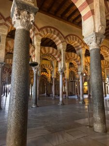 Interior view of the Great Mosque-Cathedral of Córdoba in Spain, showing rows of granite and marble columns supporting double-tiered red and beige striped arches under a wooden ceiling.