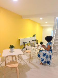 Student sitting in a bright yellow lounge area using a phone and laptop at Jaleo Madrid Spanish school.